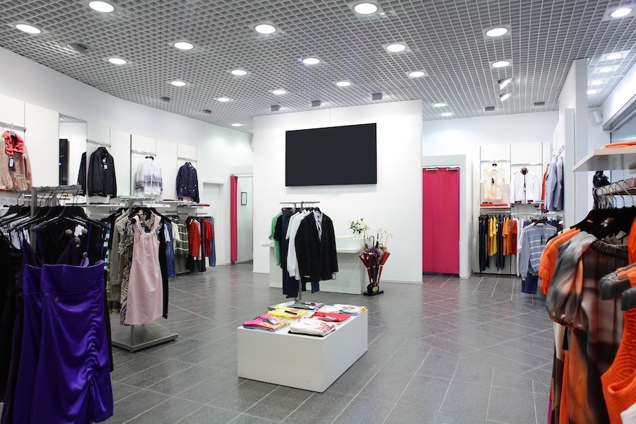 A brightly lit clothing store with a TV on a wall in the background.