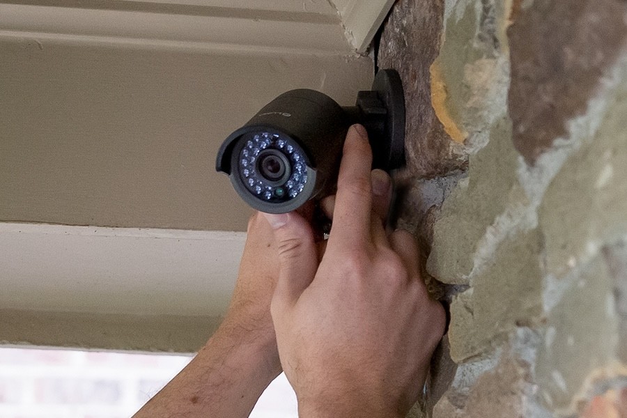 Two hands installing a security camera outdoors.