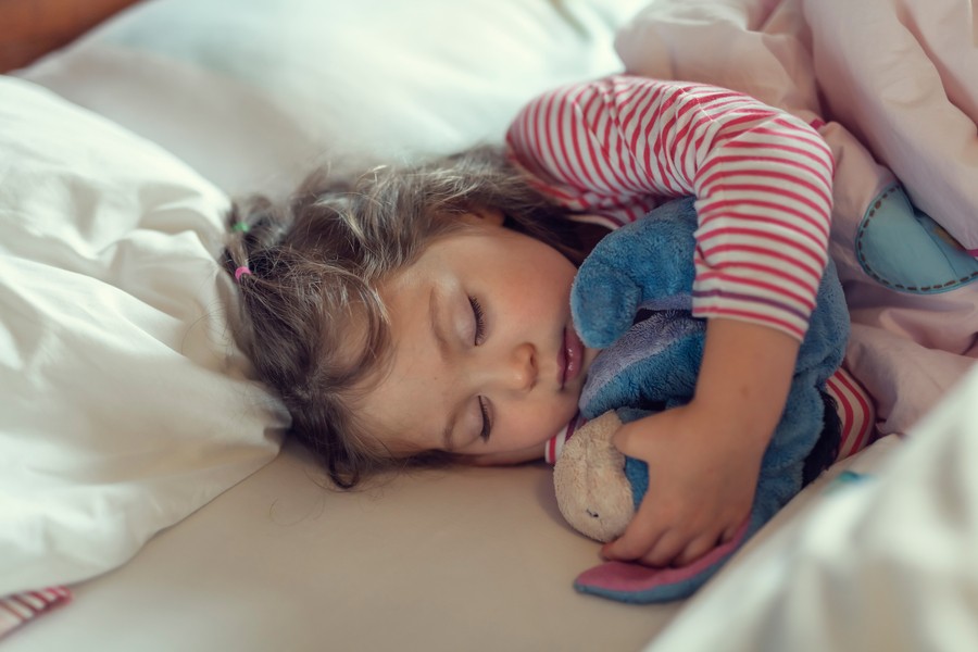 A child sleeping in a bed with a stuffed Eeyore.