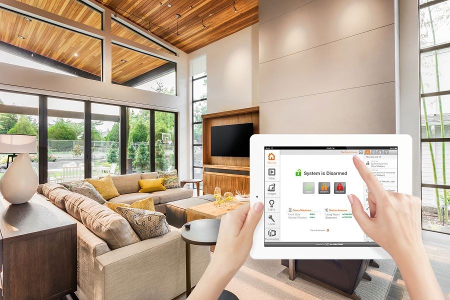 A woman’s hands holding up a tablet in the living that shows a disarmed security system.