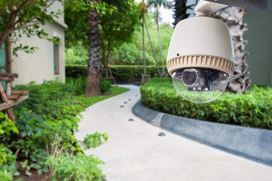 An outdoor surveillance camera sits in the foreground with a manicured path behind it.