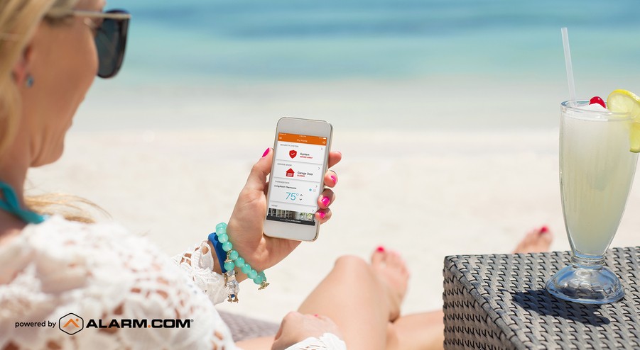 A person at a beach holding a smartphone showing the status of their home security system in Springfield, MO.